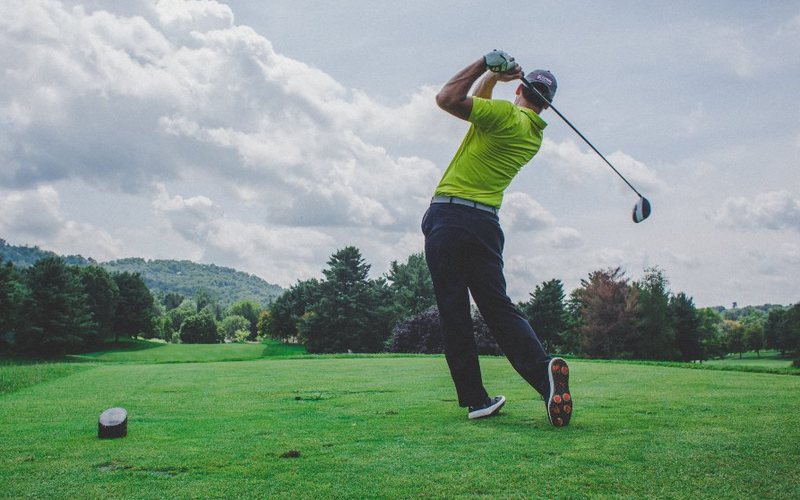 A golfer driving off the tee on a tree-lined course